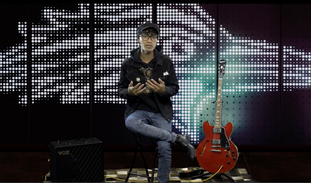 Putu Hiranmayena sitting on stage surrounded by guitar and amplifier demonstrating personalize and engaging delivery of content.