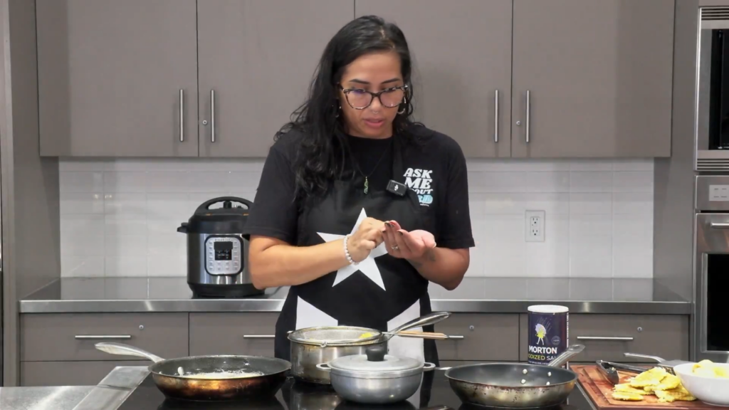 A chef engaging in a cooking demonstration in a kitchen, showing multiple pots and pans in use.